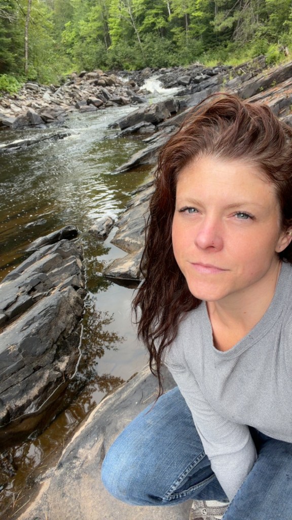 Katrina beside a rocky river in the woods.