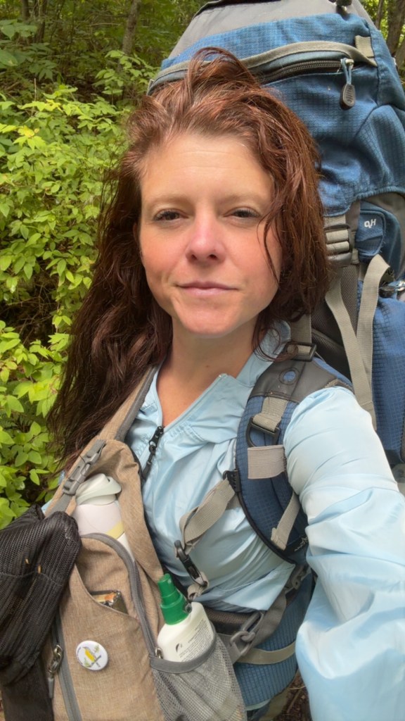 Katrina on a wooded trail with her hiking backpack.
